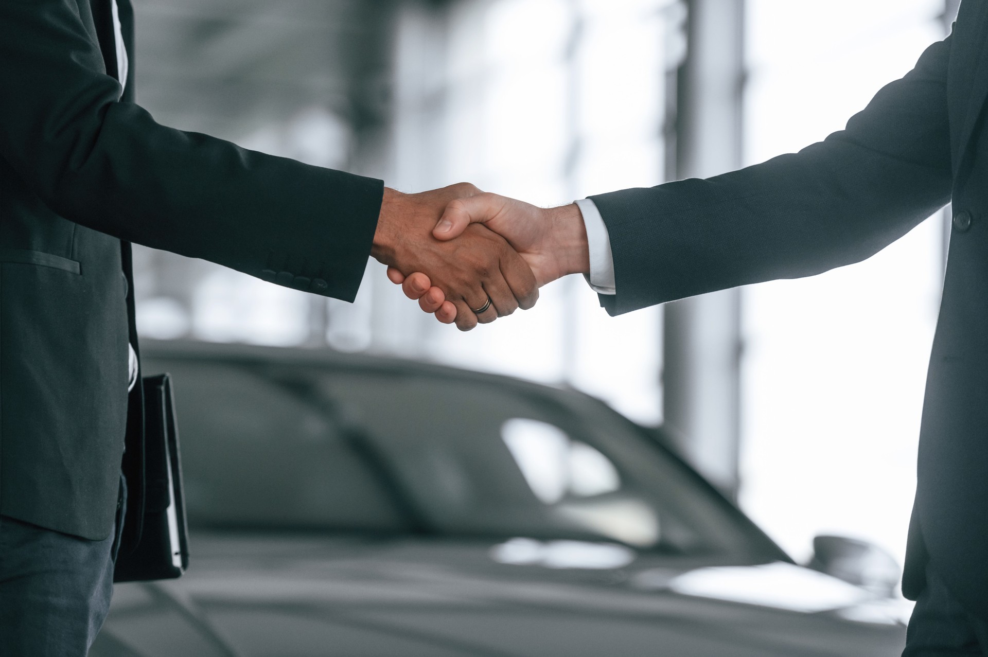Close up view. Two businessmen are standing in the car showroom and making a deal, handshake